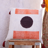 Woman in a yellow saree standing next to a white pillow with a black circle and orange design in a white archway.