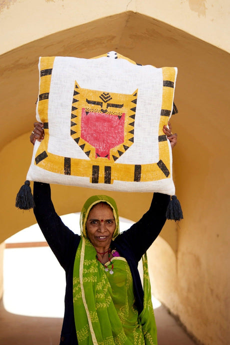Woman holding a colorful traditional pillow against a beige wall.