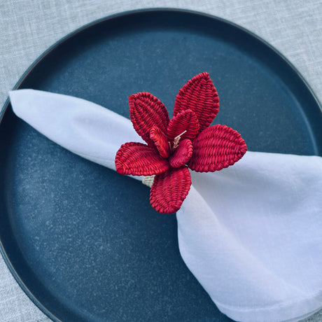 Red floral napkin ring on a white napkin over a blue plate with a gray textured background