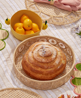 Loaf of bread on a woven plate with a basket of lemons on a textured surface