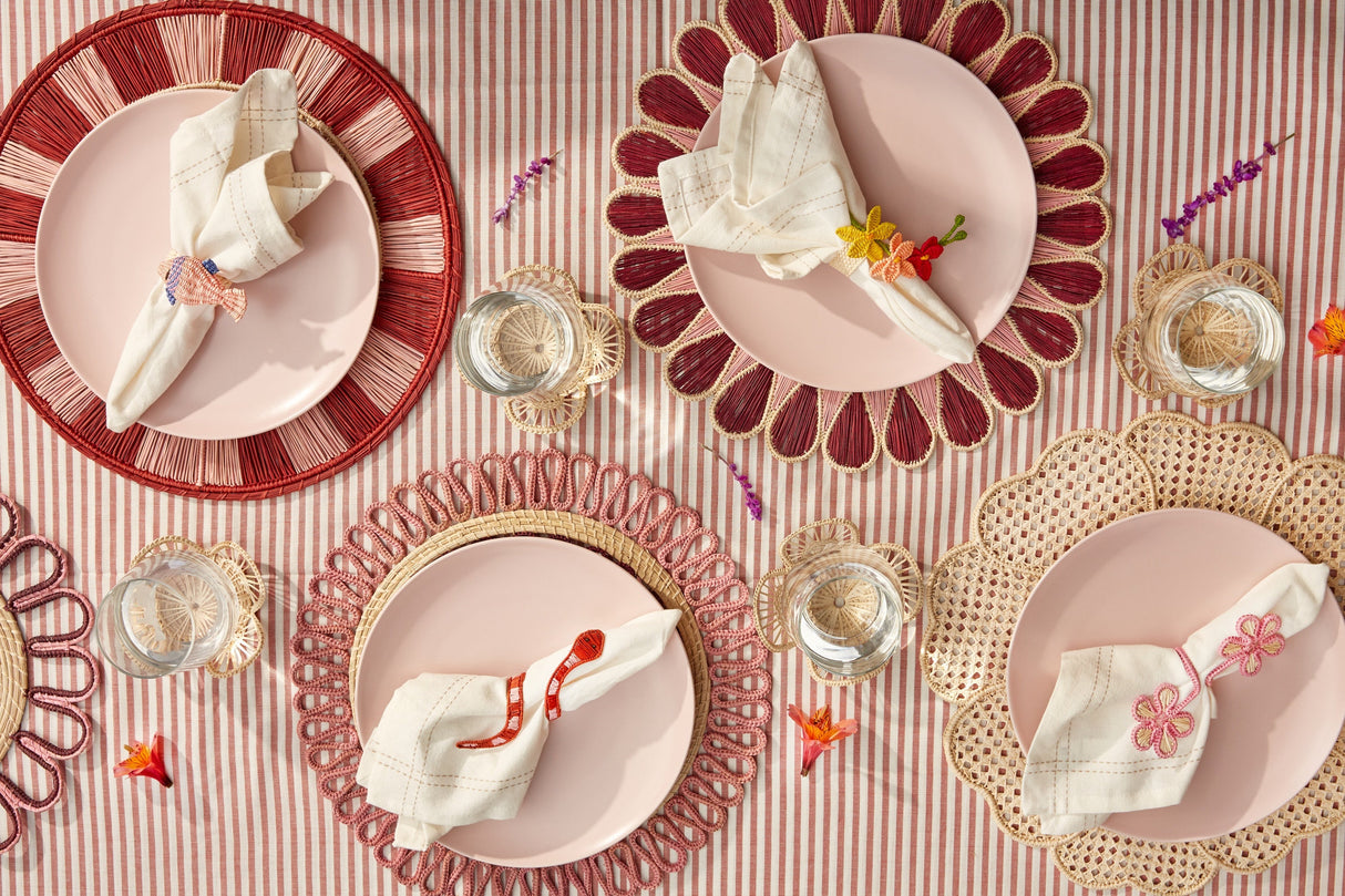 Decorative table setting with pink plates, red rimmed chargers, and floral napkins on a striped tablecloth.