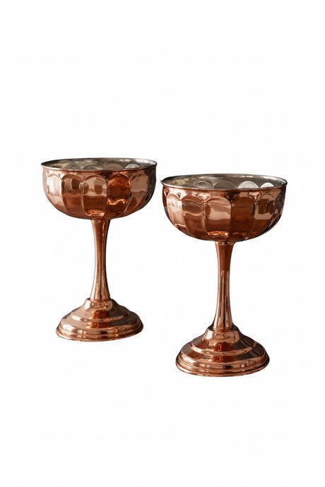 Two copper-colored cocktail glasses on a white background