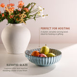 White vase with flowers and blue serving bowl with fruits on a light background