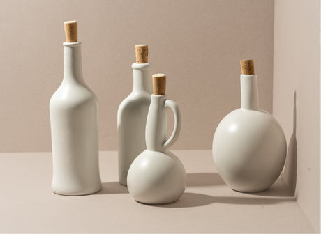 Set of white ceramic bottles with cork stoppers on a beige background