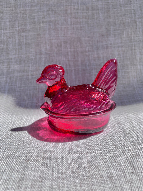 Pink glass chicken-shaped object on a gray fabric background