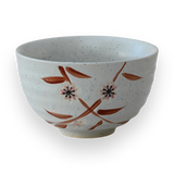 The Bamboo Matcha Bowl is a speckled white ceramic bowl featuring a painted floral design on a black background, showcasing the elegance of Minoyaki pottery, and is perfect for a traditional matcha tea ceremony.
