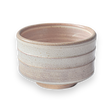 The Beige Ceramic Matcha Bowl features a textured design with subtle grooves and a wide brim, embodying traditional Japanese pottery. Its beige color against a black background enhances its elegance in simplicity, making it perfect for a matcha ritual.