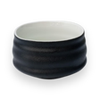 Black and white ceramic matcha bowl with a textured surface on a plain background, reminiscent of Minoyaki pottery.