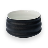 Black and white ceramic matcha bowl with a textured surface on a plain background, reminiscent of Minoyaki pottery.