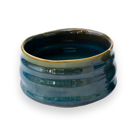 A Blue Ceramic Matcha Bowl, with a textured surface and uneven rim, sits elegantly on a black backdrop, inviting the bamboo matcha whisk to complete the timeless tea ritual.