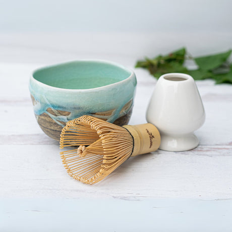 Japanese Matcha Tea Bowl with Blue & Brown Glaze, paired with a bamboo whisk and white holder, crafted using traditional Minoyaki pottery techniques, rests on a white wooden surface.