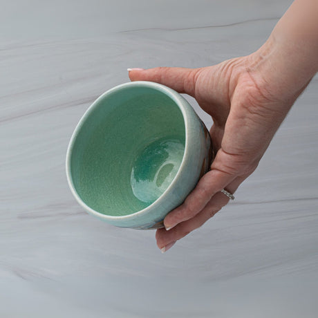 A hand holds a small, blue and brown Japanese Matcha Tea Bowl against a light gray background, showcasing the elegance of traditional Minoyaki pottery techniques.