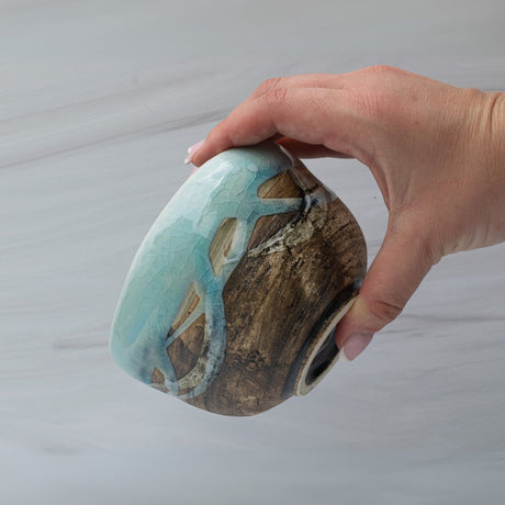 A hand holds a Japanese Matcha Tea Bowl with a Blue & Brown Glaze crafted using Minoyaki pottery techniques on a light surface.
