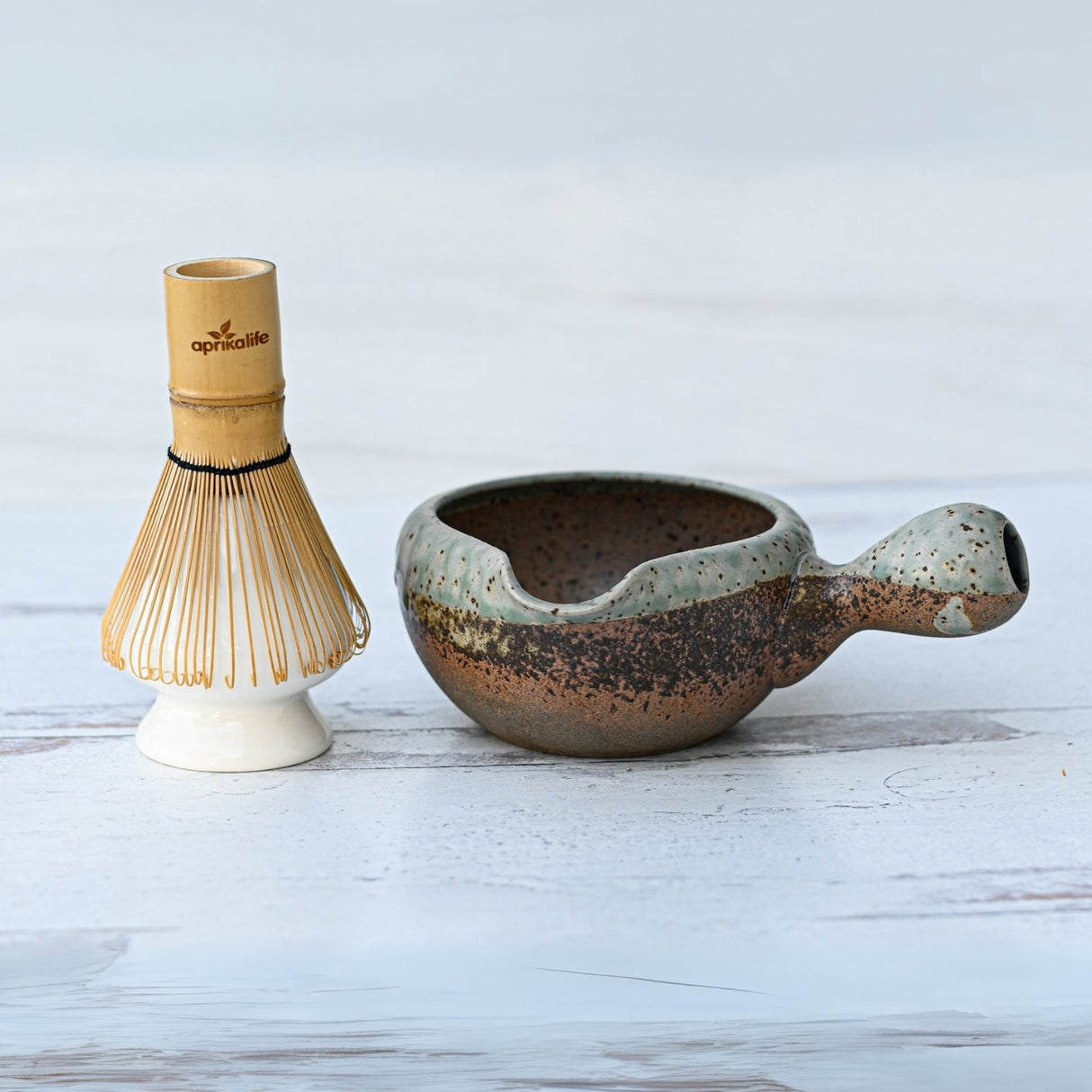 The Brown Ceramic Matcha Bowl with Spout and Bamboo Matcha Whisk from the Organic Japanese Matcha Set provides an authentic tea ceremony experience on a light wooden surface.
