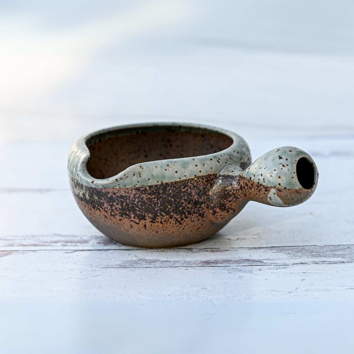 Brown ceramic matcha bowl with a handle, reminiscent of an organic Japanese set, rests on a light surface.