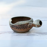 Brown ceramic matcha bowl with a handle, reminiscent of an organic Japanese set, rests on a light surface.