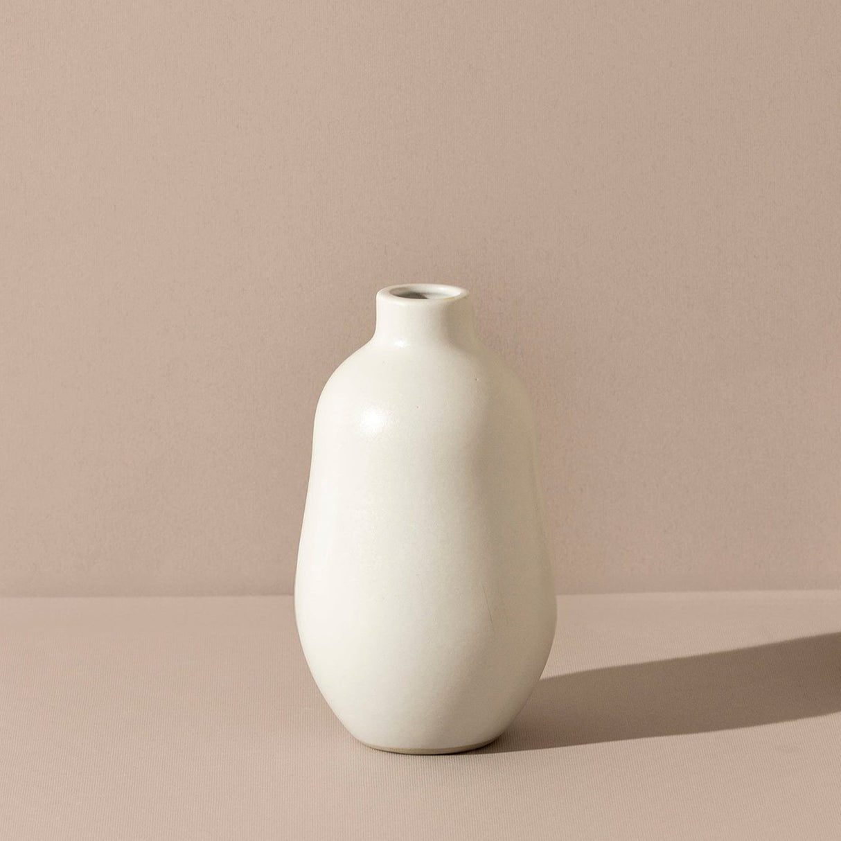 White vase on a beige surface with a pinkish-beige background