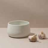 White ceramic bowl on a beige surface with two garlic bulbs.