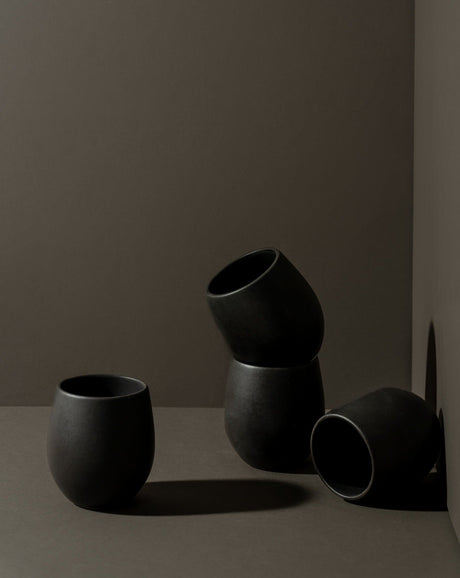 Black ceramic cups on a gray surface with a dark brown background