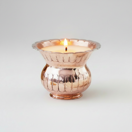 Candle in a copper holder on a light gray background