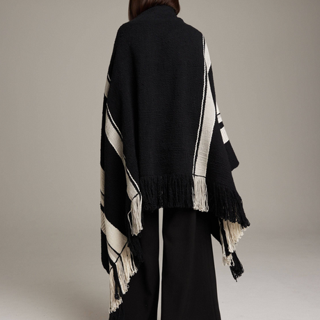 Black and white striped poncho with fringe details on a neutral background