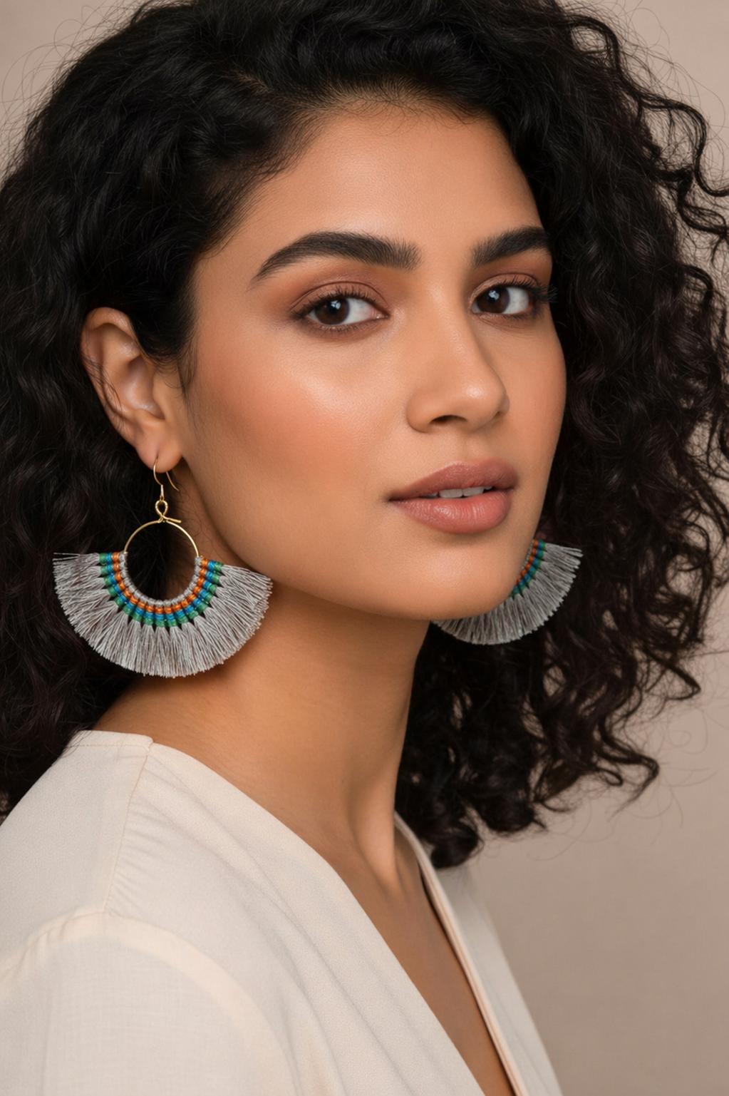 Woman wearing large, decorative earrings against a neutral background