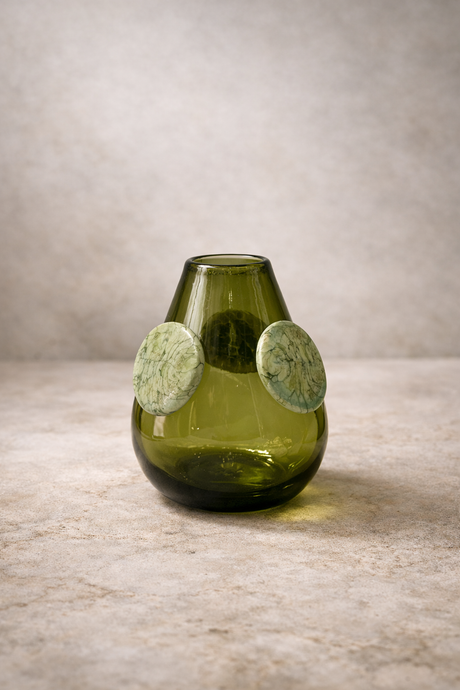 Green glass vase with circular decorations on a wooden surface