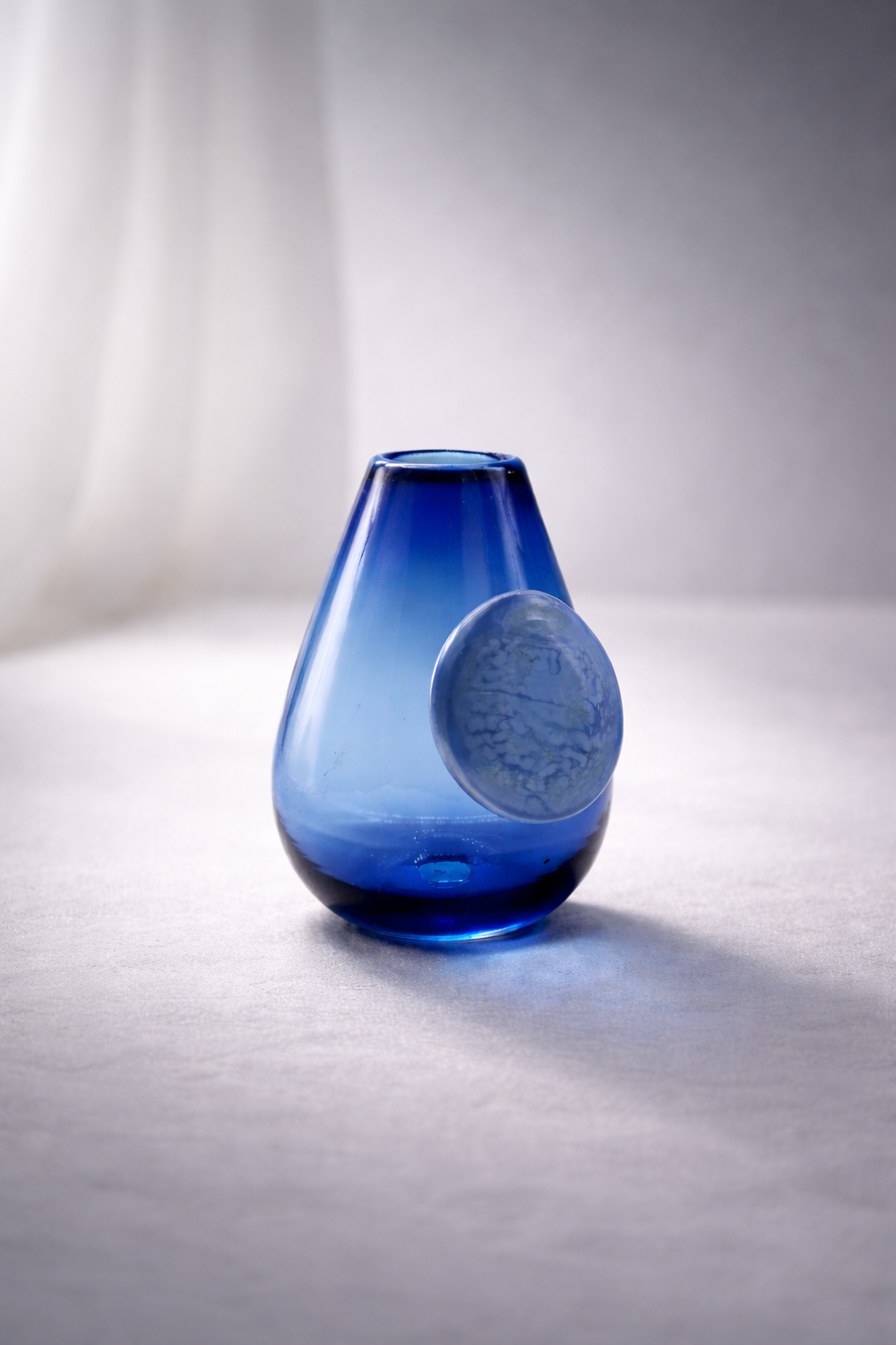 Blue glass vase on a light gray surface with a blurred white background