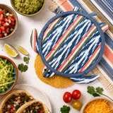 Colorful striped pot holder on a table with taco ingredients and a striped placemat.