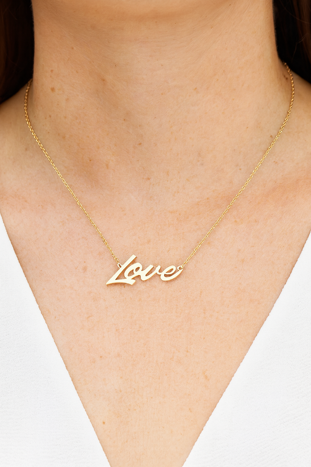 Gold 'Love' necklace on a person's neck against a neutral background
