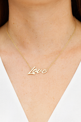 Gold 'Love' necklace on a person's neck against a neutral background