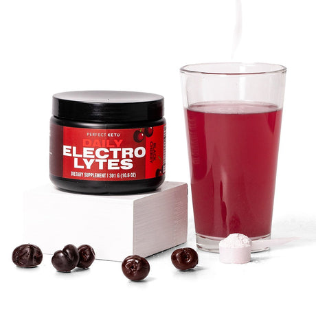 Perfect Keto Daily Electrolytes supplement jar with a glass of red liquid and cherry candies on a white background