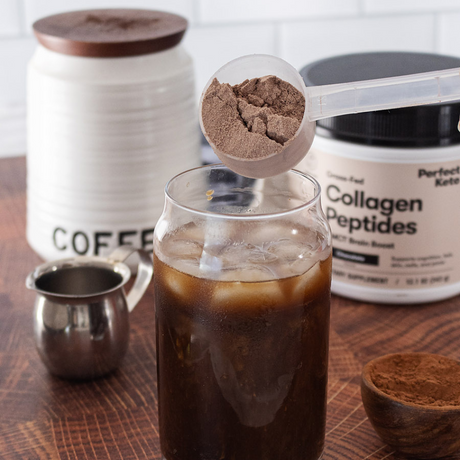 Collagen peptides being added to iced coffee with a container of Perfect Keto Collagen Peptides in the background.