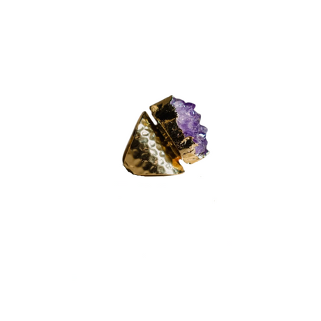 Ring with gold band and purple gemstone on a beige stone base against a white background