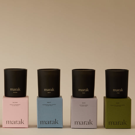 Four black candles on colorful boxes with 'marak' branding against a beige background. Collection Votive Set | 3.4oz Soy Wax Scented Candles