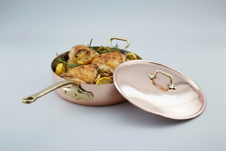 Copper cookware with chicken dish on a light gray background