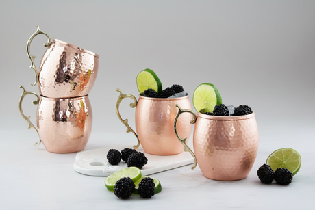Copper mugs with blackberries and lime wedges on a light gray background