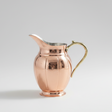 Copper pitcher with a gold handle on a light gray background
