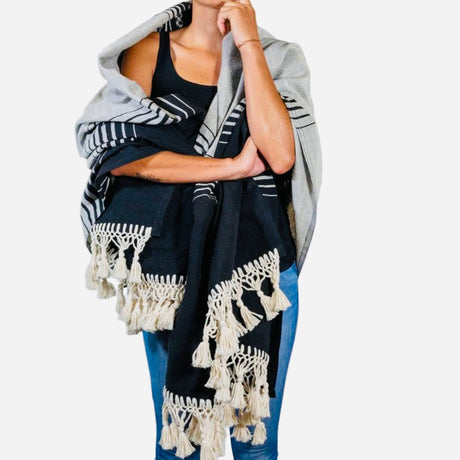 Person wearing a black and gray patterned scarf with tassels on a white background