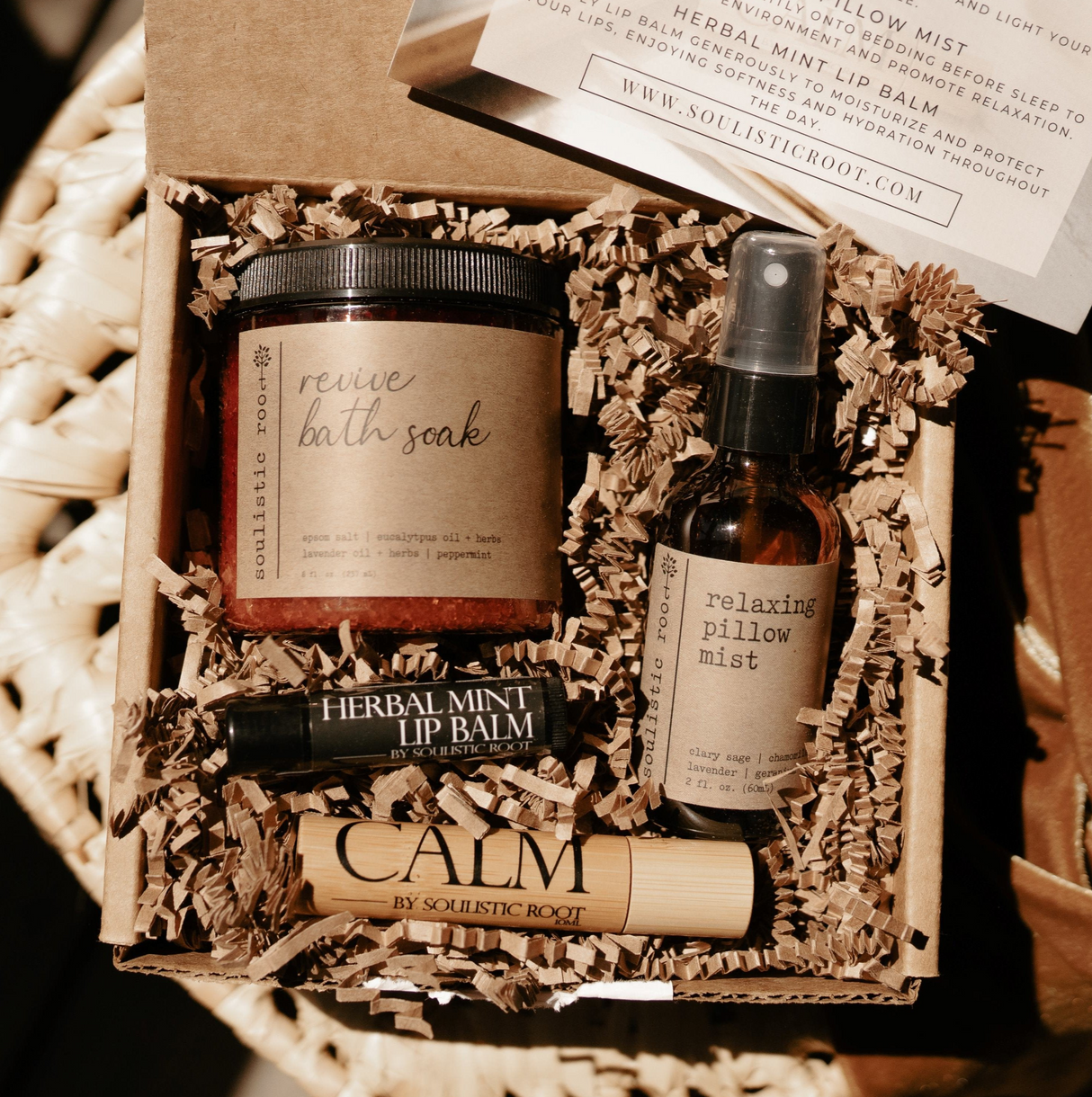 Set of natural skincare products including a bath soak, lip balm, and pillow mist in a decorative box.
