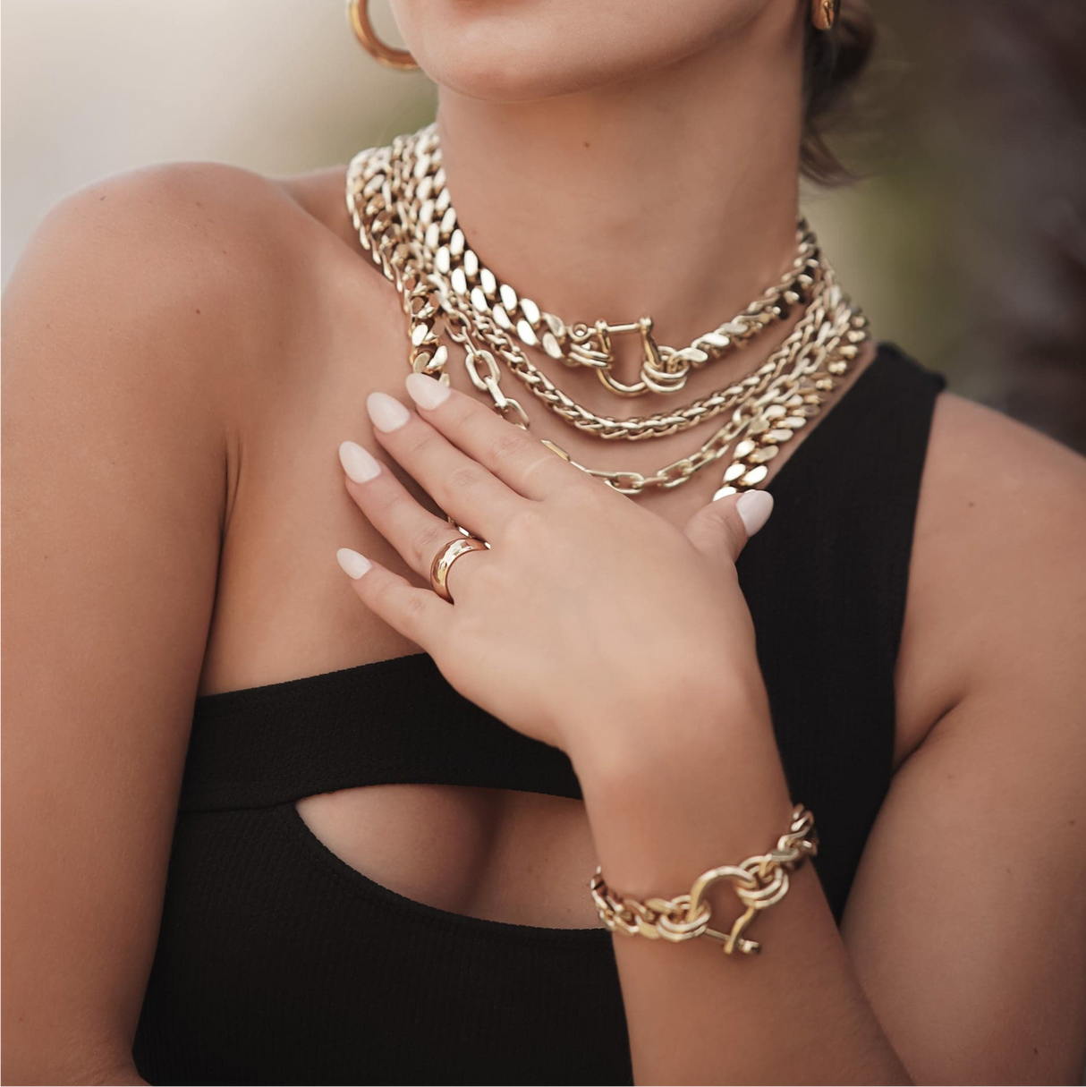 Woman wearing multiple gold chains, bracelets, and rings on a blurred background