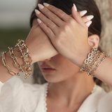 Close-up of a person wearing multiple gold chain bracelets on a blurred background