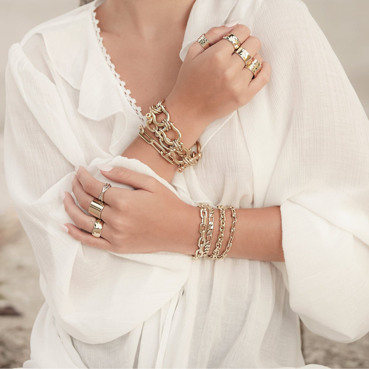Gold jewelry including bracelets and rings on a white outfit