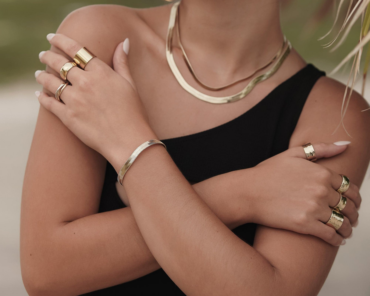Close-up of a person wearing gold jewelry including necklaces, bracelets, and rings.
