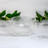 Textured Spouted Glass Matcha Bowl Pattern 2 with bamboo matcha whisk and whisk holder set—a stylish set featured on a light surface with green leaves in the background, perfect for elevating your matcha experience.