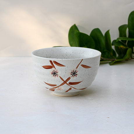 Bamboo Matcha Bowl with floral design on a light background, complemented by a Bamboo Matcha Whisk and scattered green leaves.