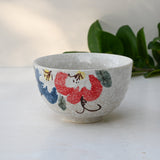 A Minoyaki ceramic matcha bowl featuring red and blue flowers with subtle leaves in the background.
