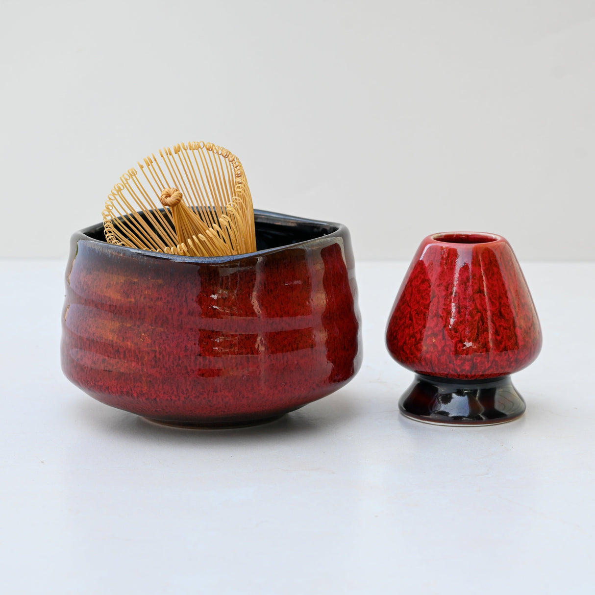 The Red Matcha Bowl and Bamboo Whisk from the Matcha Set are perfect with a small matching vase on a white surface, all beautifully crafted in Minoyaki pottery style.