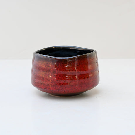 The Red Matcha Bowl resembles traditional Minoyaki Pottery with a textured red ceramic and black interior, elegantly resting on a white surface.