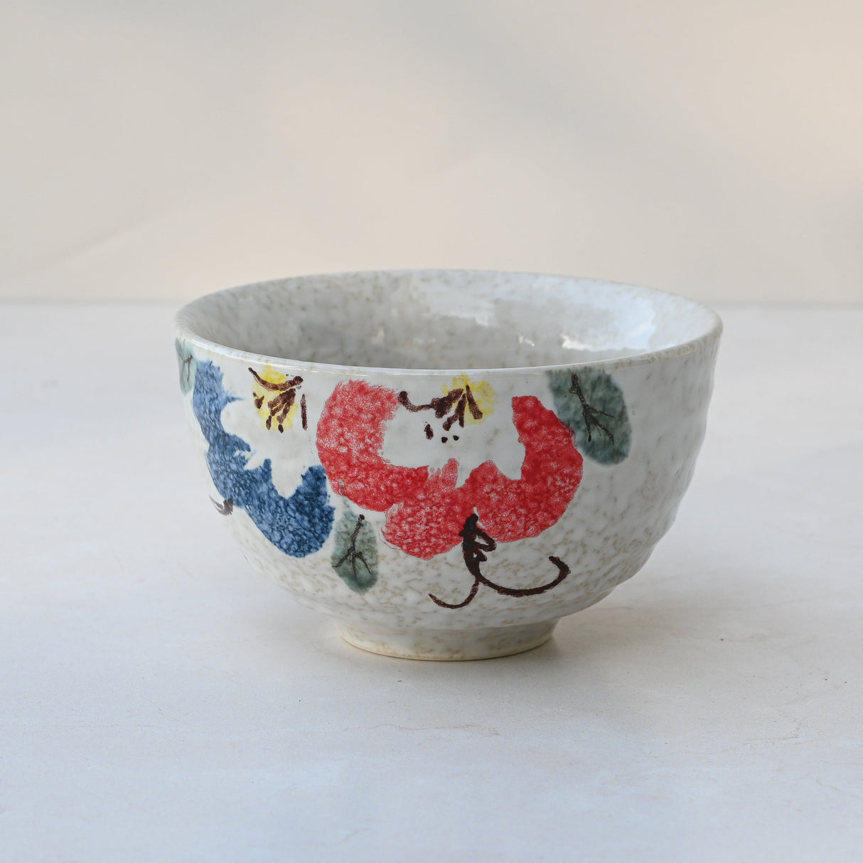 This Red and Blue Flowers Matcha Bowl features a floral design on a light background, crafted with traditional Minoyaki pottery techniques.
